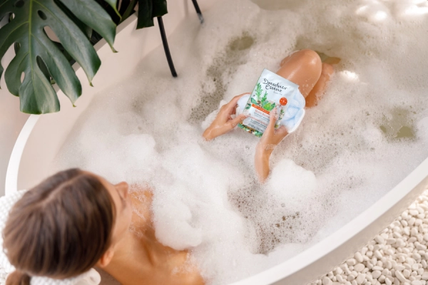 Eine Frau liegt in der Badewanne und schaut sich die Verpackung eines Dresdner Essenz Produktes an.