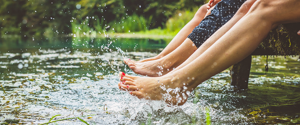Mehrere Personen sitzen an einem Steg und halten ihre Fuesse ins Wasser.