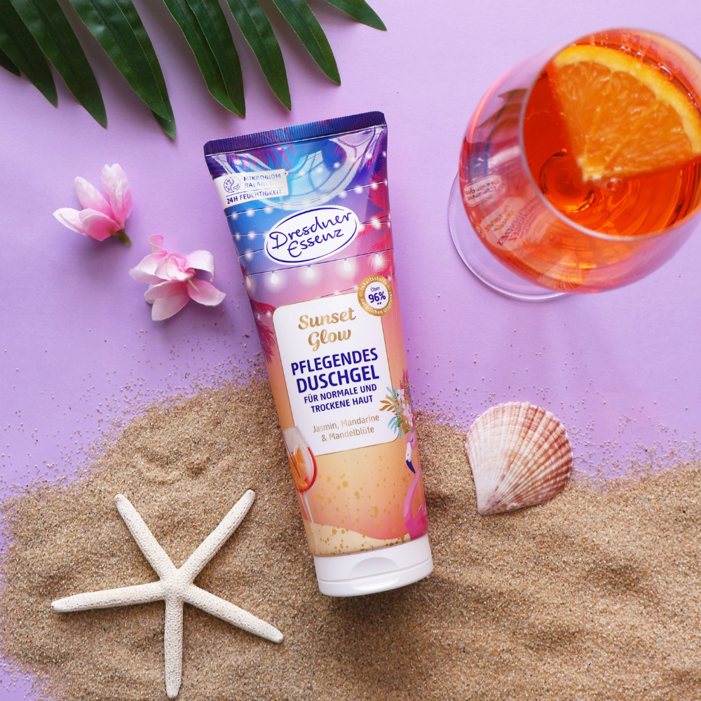 Das Duschgel liegt im Sand und ist drum herum dekoriert mit Muscheln und einem Seestern, Blueten und einem Cocktail.