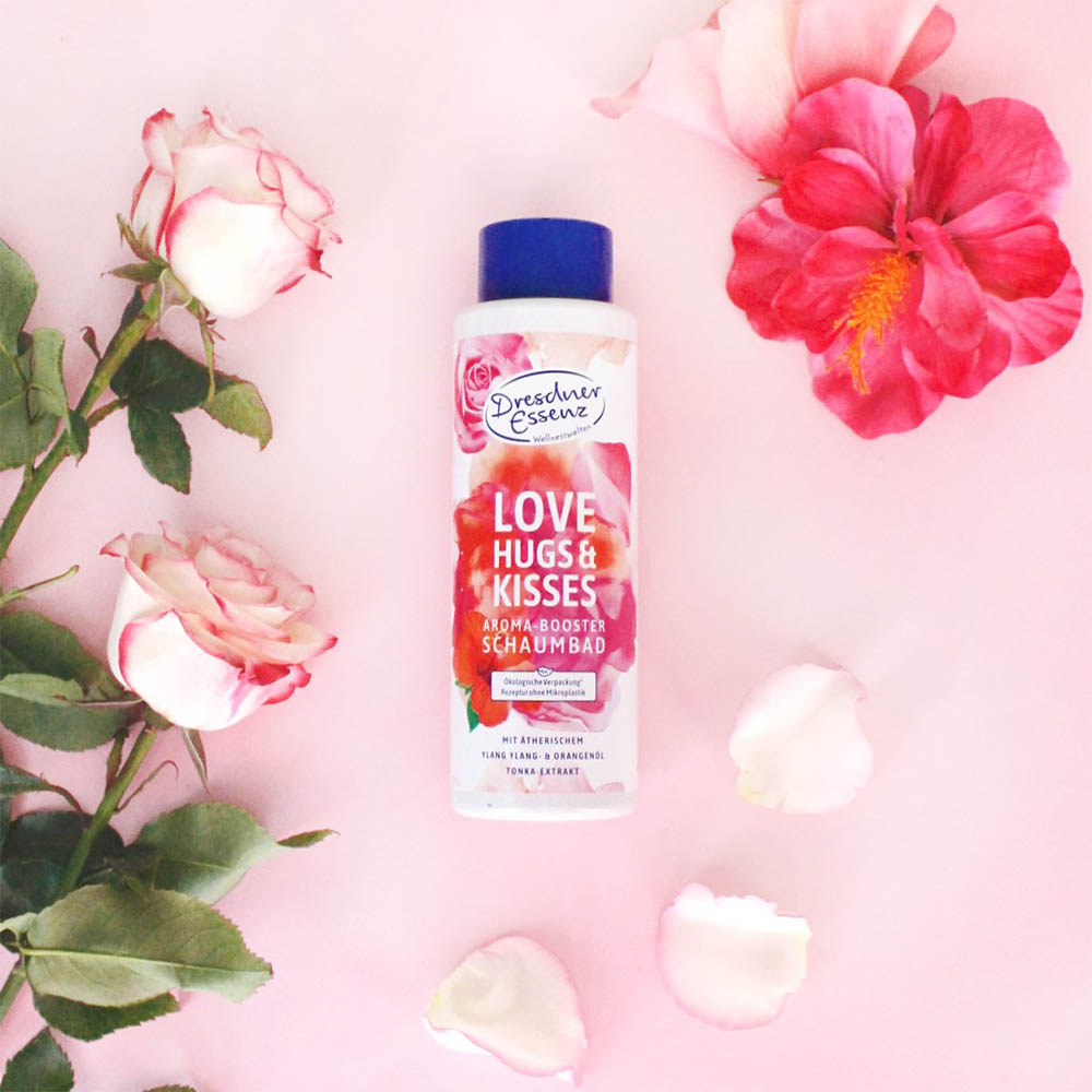 Aroma-Booster Schaumbad "Love, Hugs & Kisses" liegt zwischen verschiedenen Blumen und Blueten