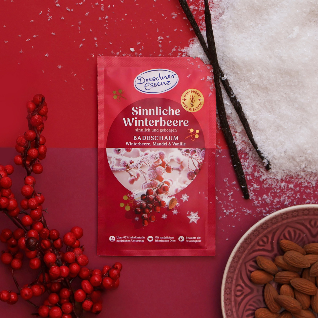 Der Badeschaum Sinnliche Winterbeere liegt zwischen Schnee, Mandeln, Vanillestangen und Winterbeeren.