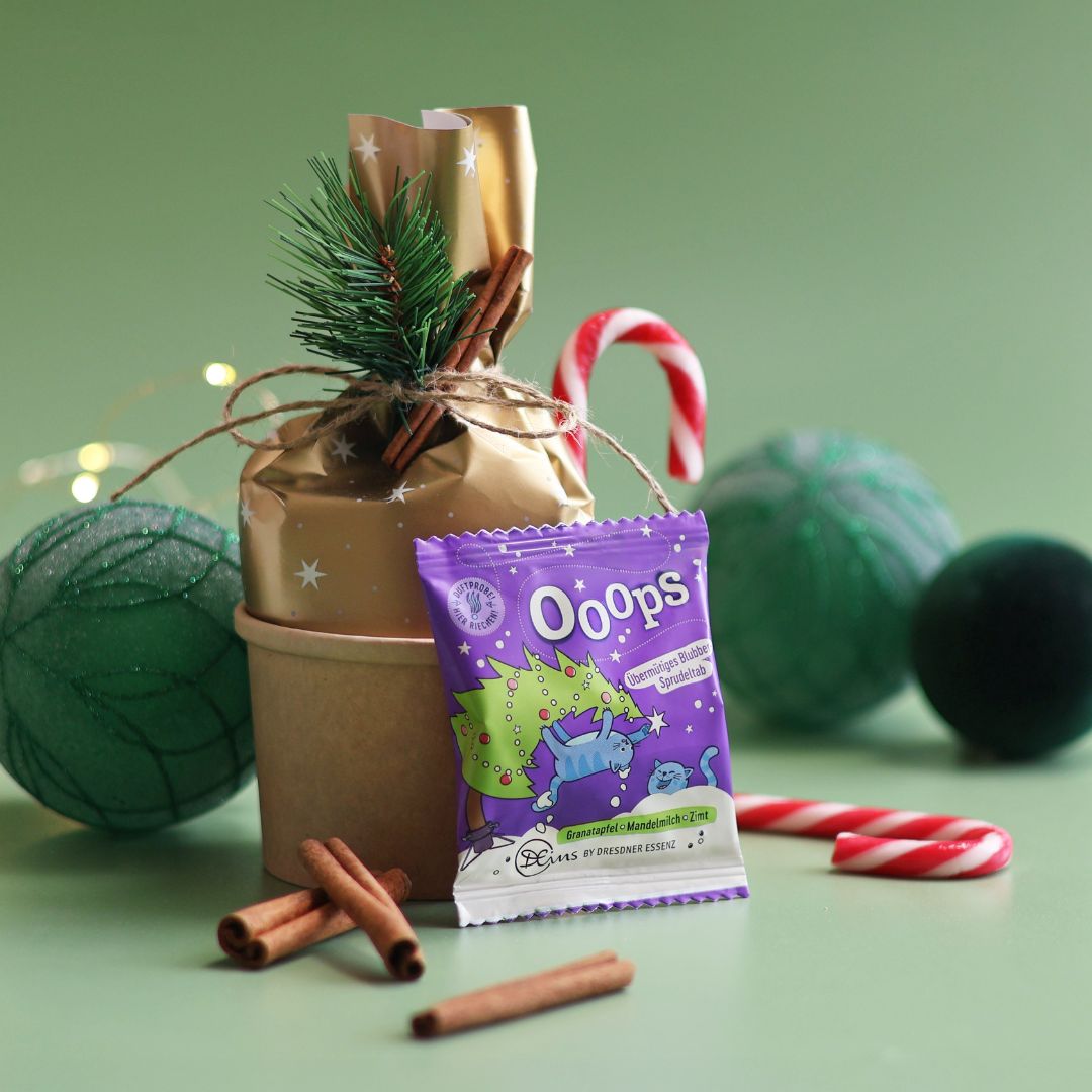Der Sprudeltab Ooops ist gegen ein kleines Geschenk gelehnt und ist drum herum dekoriert mit Zimtstangen, Zuckerstangen und Weihnachtskugeln.