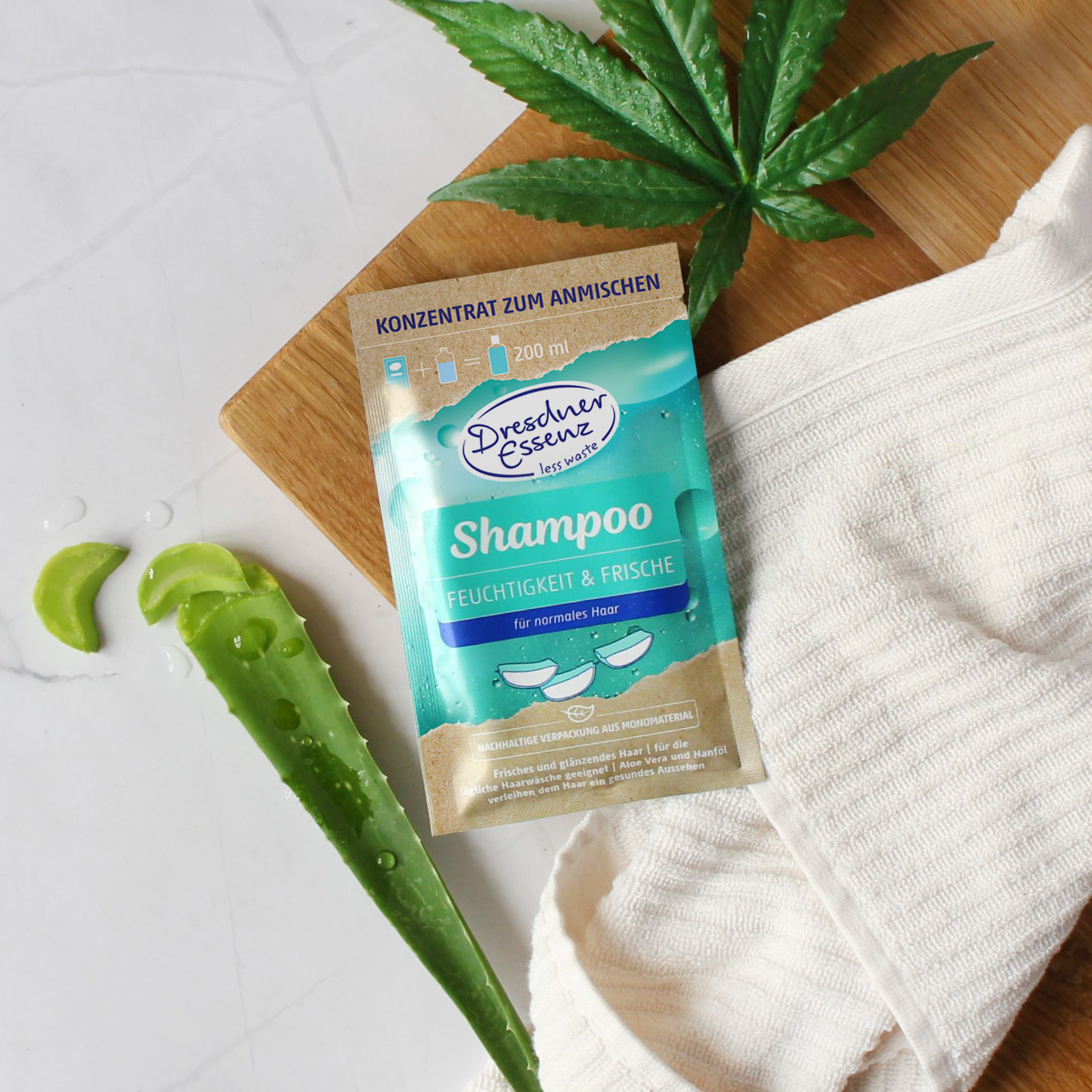 Produkt liegt auf einem Holztablett neben einem weissen Handtuch, Hanf und Aloe Vera