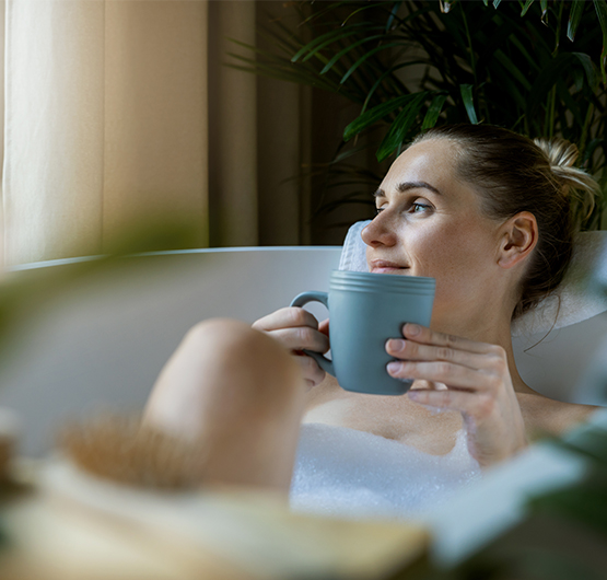Eine Frau liegt mit einer Tasse in der Badewanne und entspannt sich.