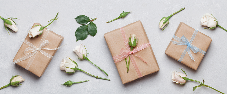 Abbildung verschiedener verpackter Geschenke, die mit weissen Rosen verziert sind.