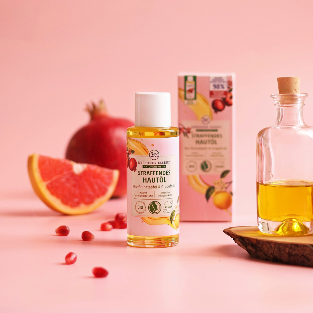 Das Hautoel steht im Fokus und ist drum herum dekoriert mit Granatapfel und Granatapfelkernen, Grapefruit und einer Flasche mit Oel.