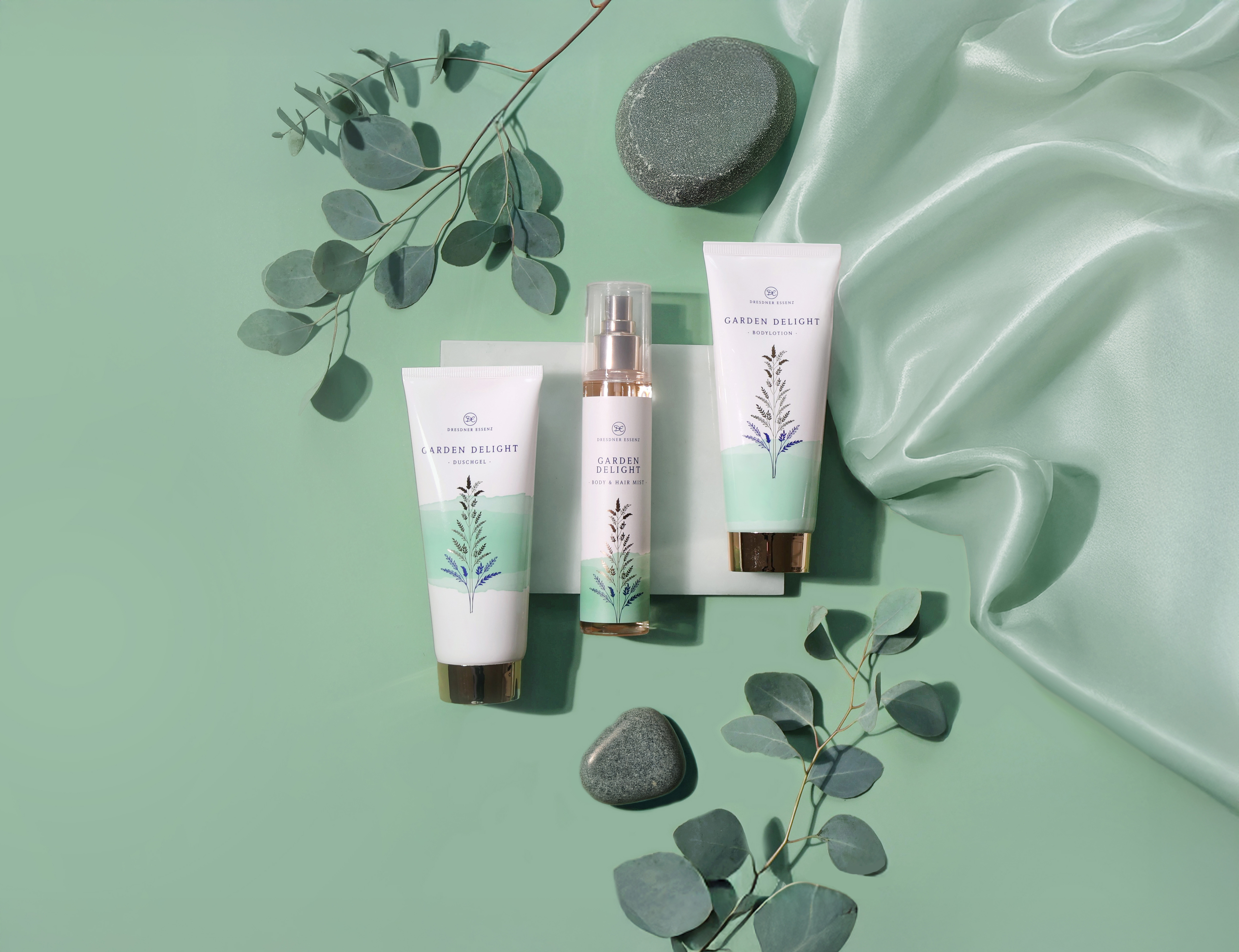 Die drei Produkte der Garden Delight Serie liegen nebeneinander und sind drum herum dekoriert mit Pflanzen, Blaettern und edlen Stoffen.