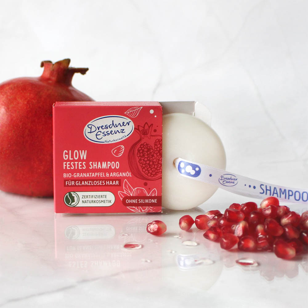 Festes Shampoo steht neben Granatapfelkernen auf einem marmorierten Untergrund