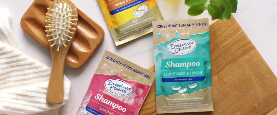 Drei Less Waste Shampoos liegen auf einem holzigen Untergrund. Daneben lieget eine Holzbuerste und ein Handtuch.
