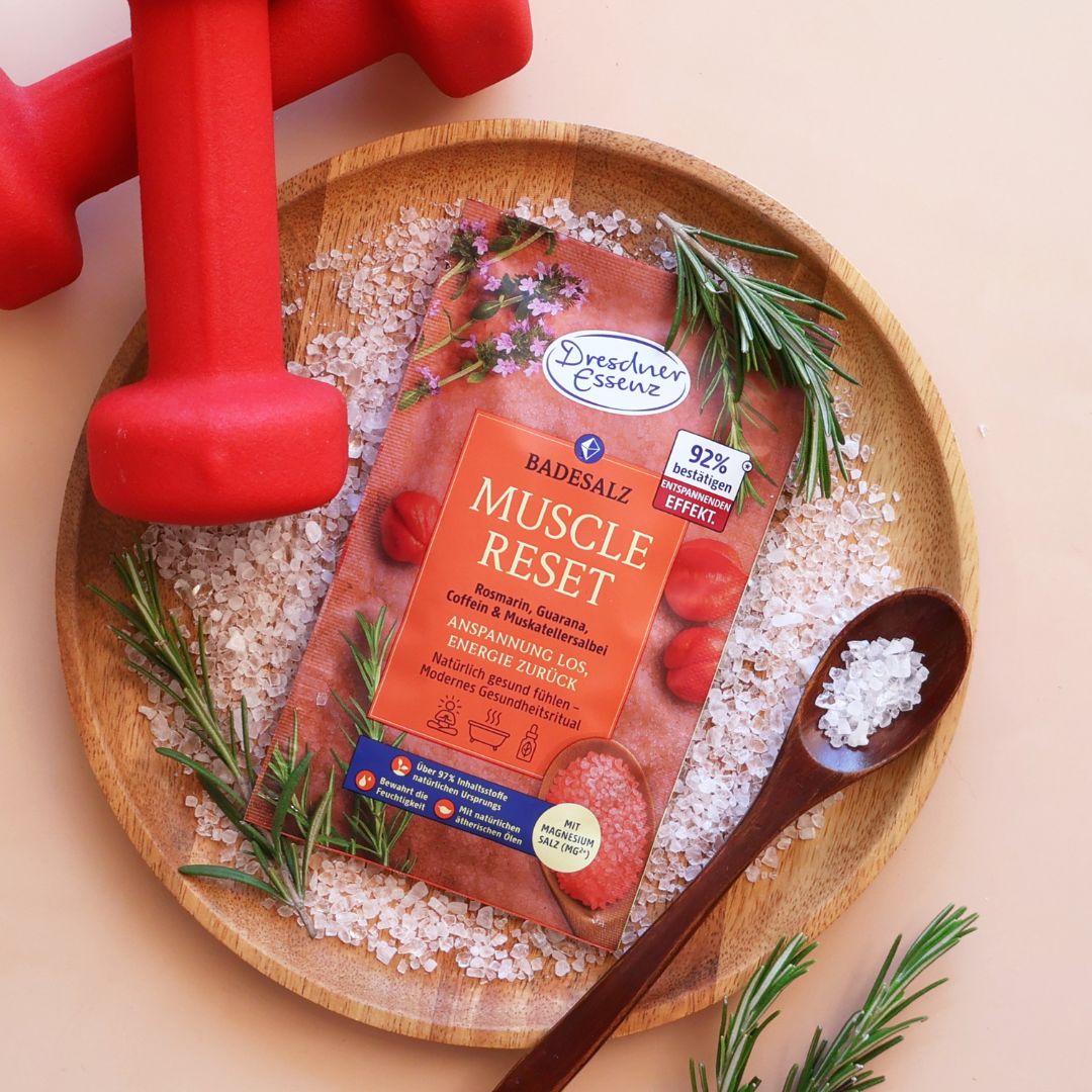 Das Badesalz Muscle Reset liegt auf einem Holzteller und ist mit Hanteln und Rosmarin dekoriert.
