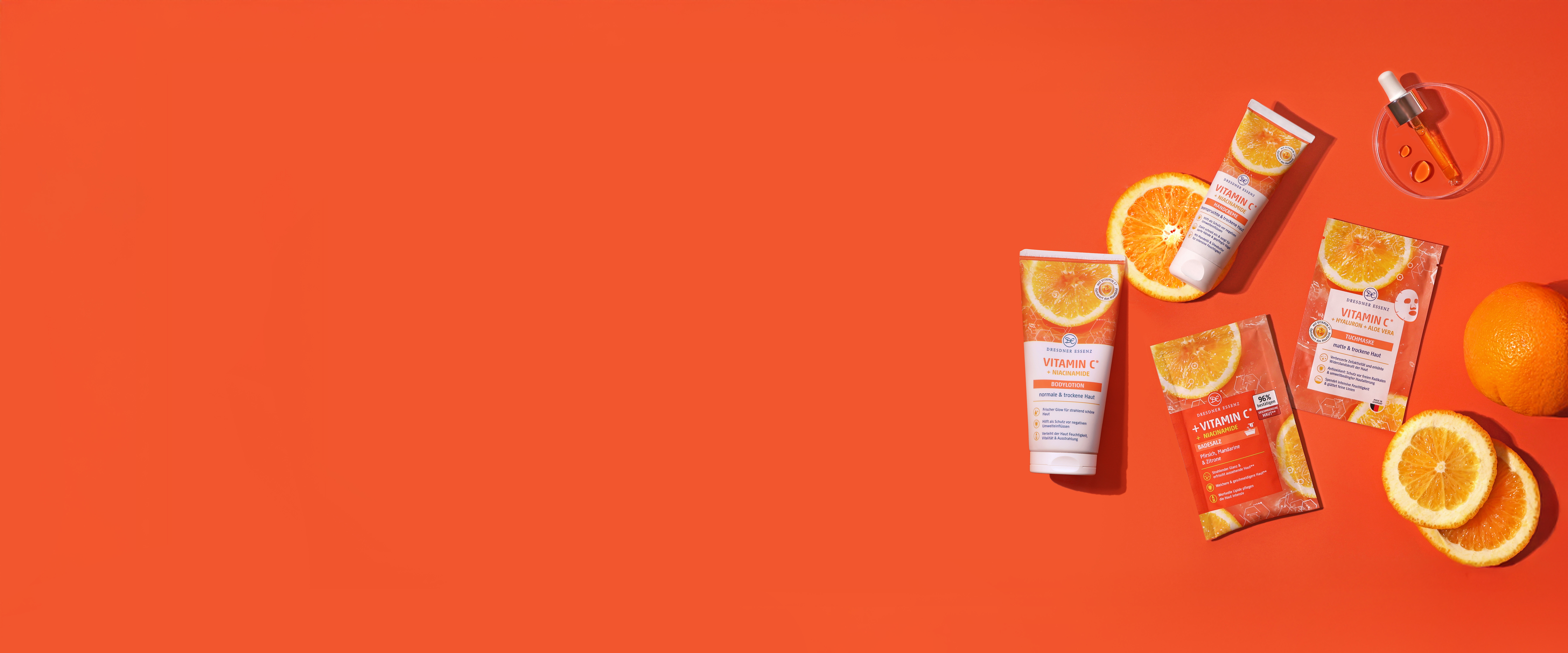 Die Produkte Badesalz, Tuchmaske, Handcreme und Bodylotion aus der Vitamin C Serie liegen nebeneinander und drum herum liegen dekorativ Orangen und Orangenscheiben und eine Pipette.