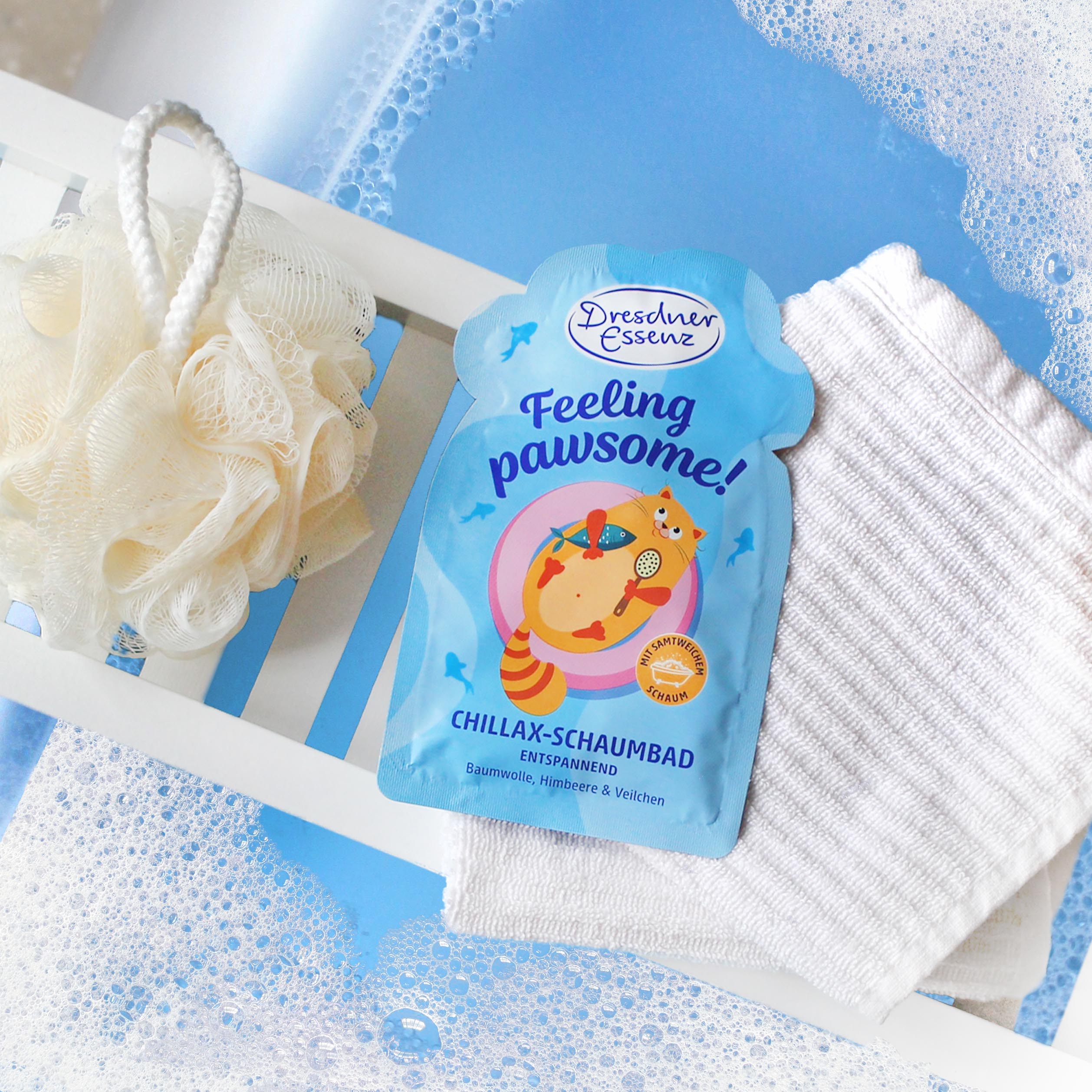 Schaumbad liegt auf einer Badewannnenablage neben einem kleinen Handtuch und einem Badeschwamm. Das Wasser in der Wanne schaeumt und ist blaeulich verfaerbt.