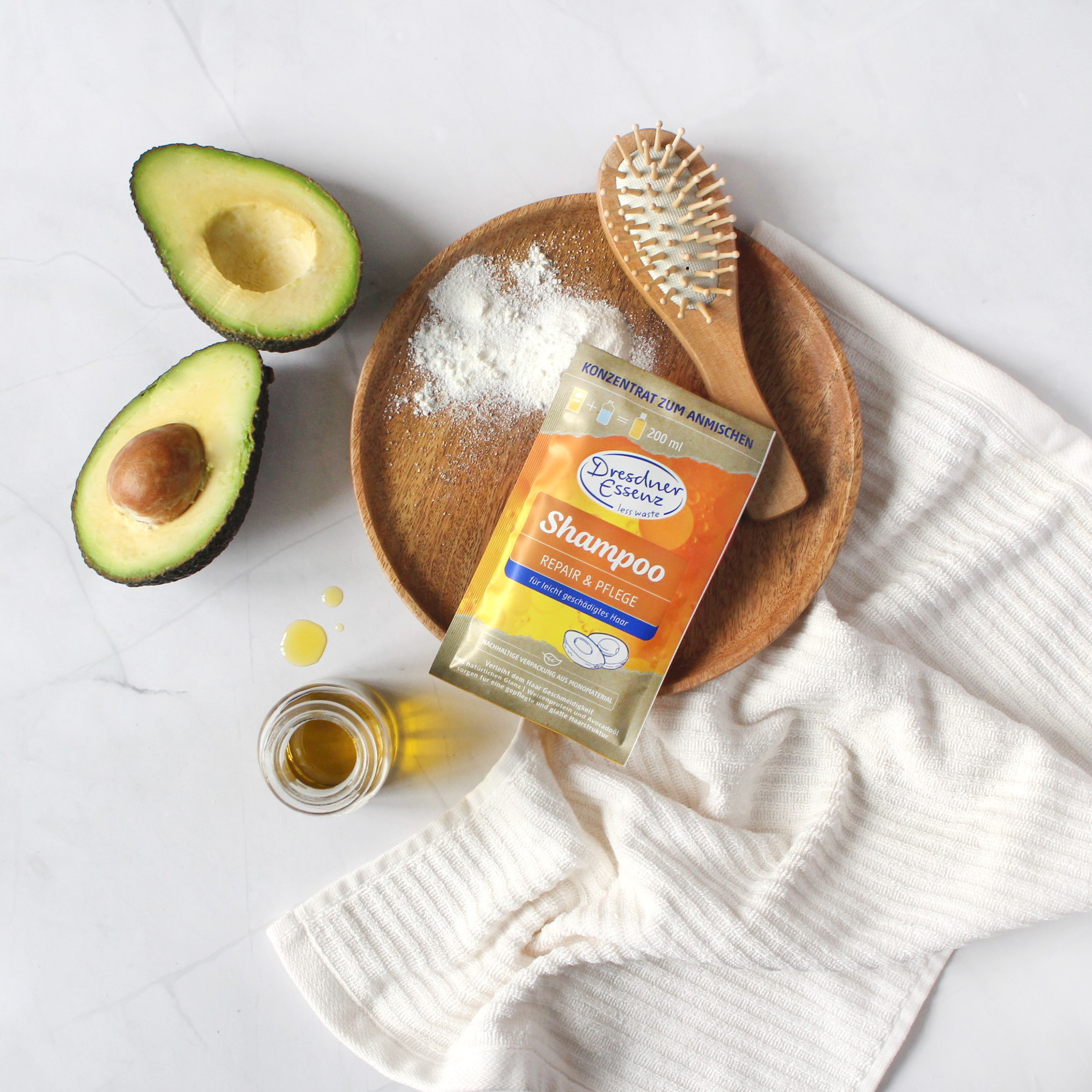 Shampoo Konzentrat Repair & Pflege liegt auf einem Holztablett neben einer aufgeschnittenen Avocado und einer Holzbuerste
