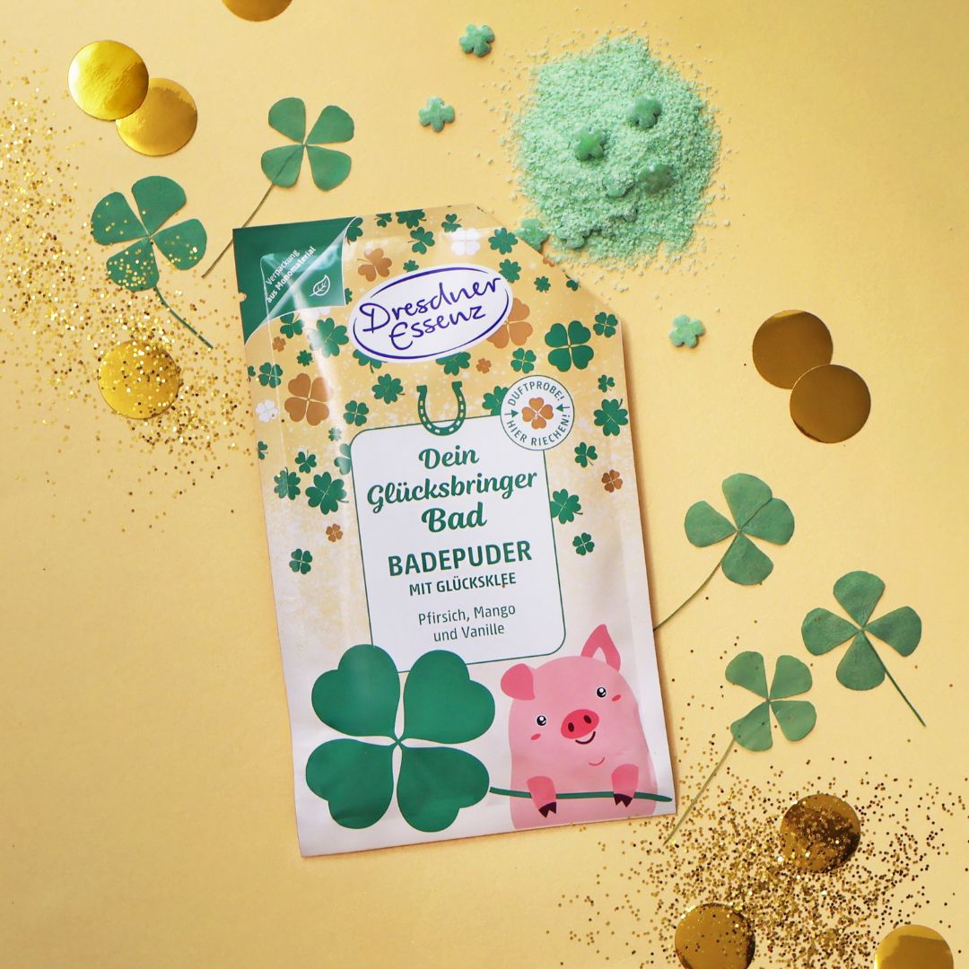 Das Produkt ist geöffnet und das gruene Badepuder ein wenig verstreut. Drum herum liegen kleine Kleeblaetter und goldenes Konfetti