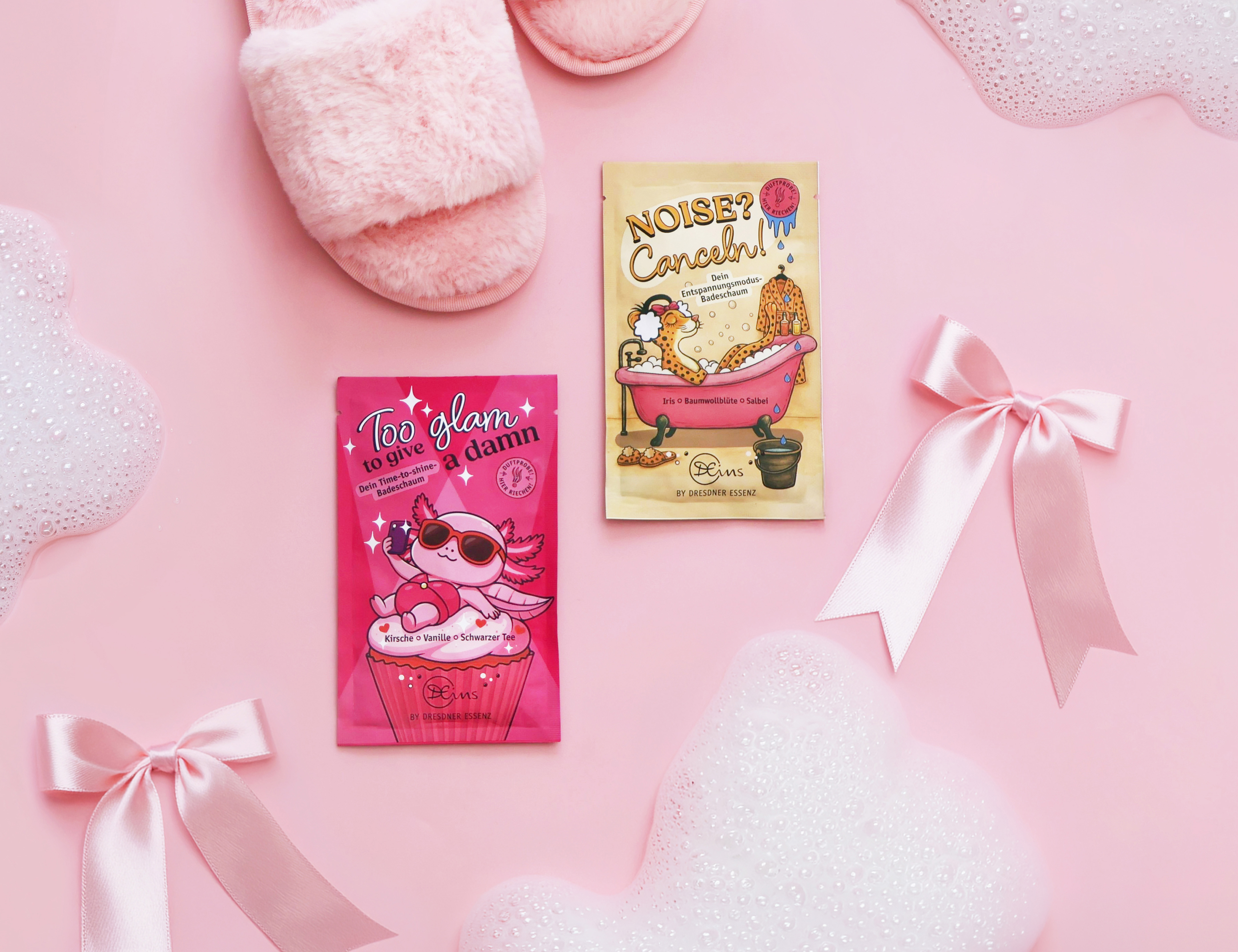 Anordnung der beiden Produkte zwischen rosafarbenen Schleifen und passenden Duft-Elementen, wie Kirschen, Vanille und Baumwollblüten