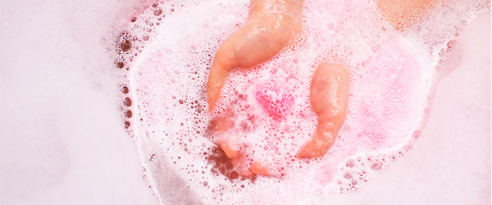 eine pinke Badekugel wird in Wasser gelassen und loest sich auf