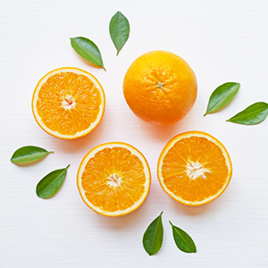 Orangenscheiben sowie eine ganze Orange liegen nebeneinander und sind rings herum dekoriert mit verschiedenen Blaettern
