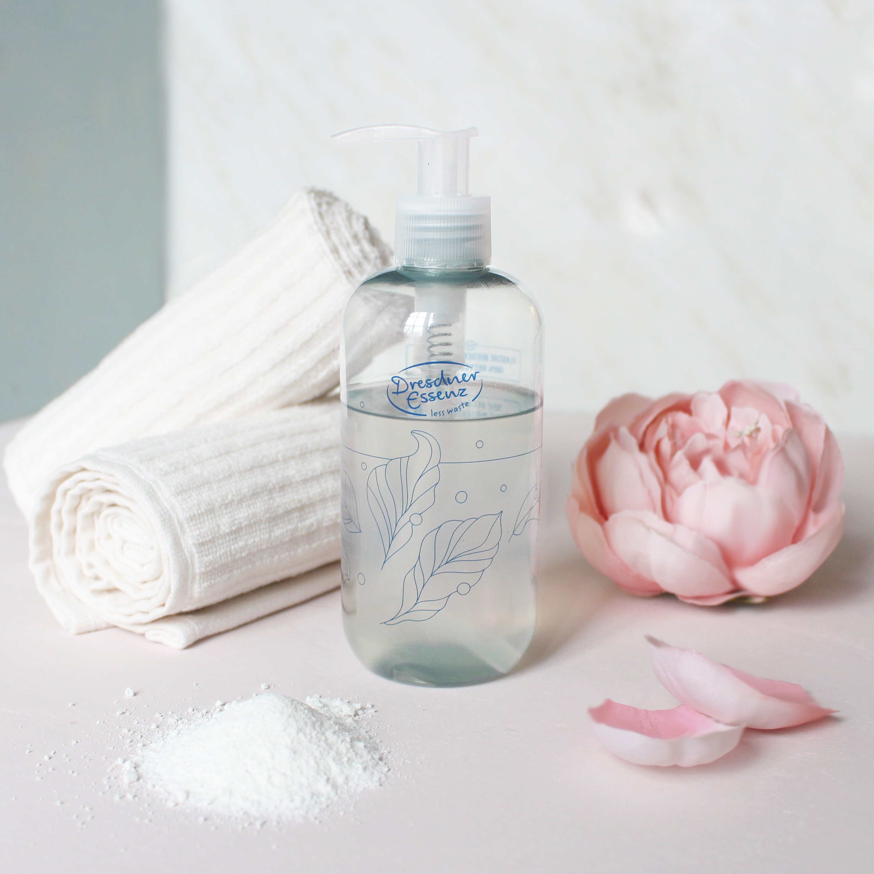 Less Waste Flasche ist mit einem Produkt befüllt; drum herum liegen Hnadtücher und Dekoblüten
