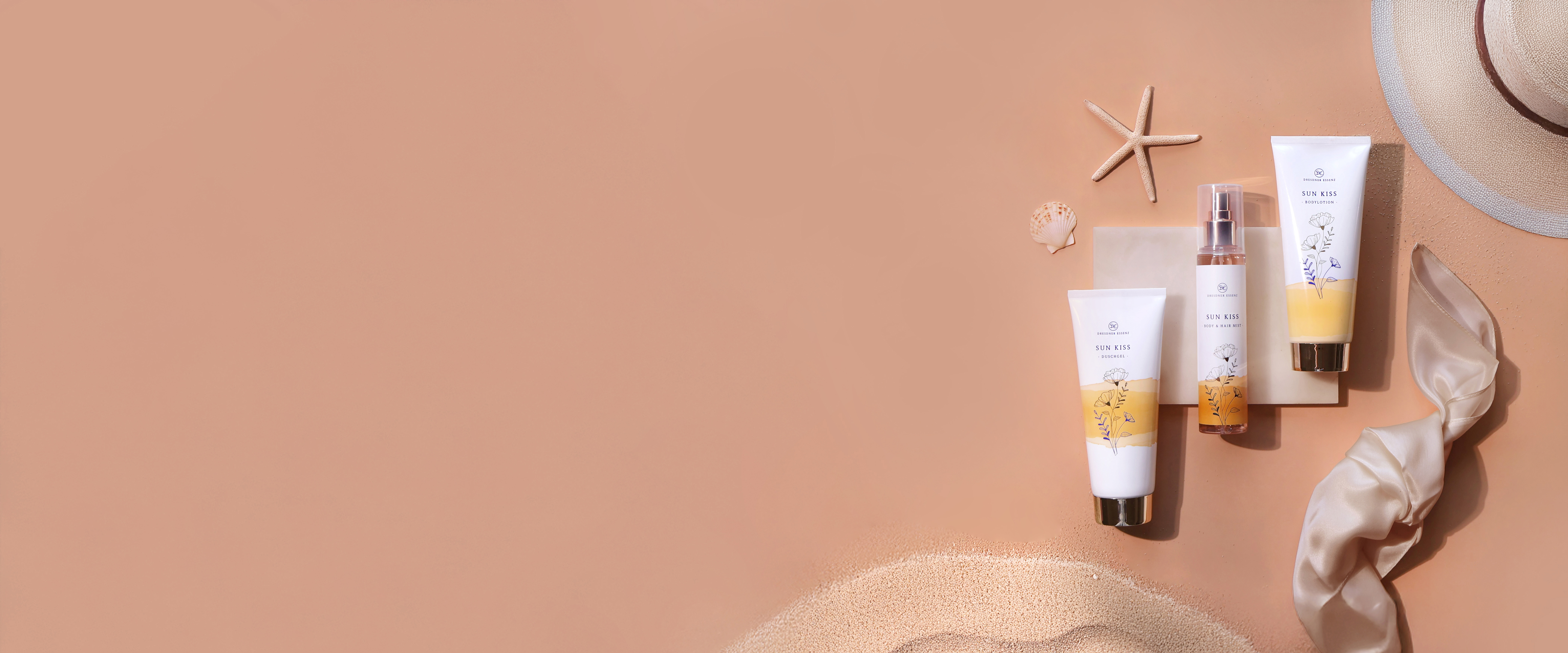 Die drei Produkte der Sun Kiss Serie liegen nebeneinander und sind drum herum dekoriert mit Seesternen, Muscheln, Sand, einem Sonnenhut und edlen Stoffen.