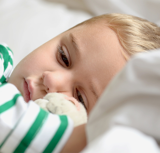 Ein krankes Kind liegt eingekuschelt im Bett und schaut verstimmt..