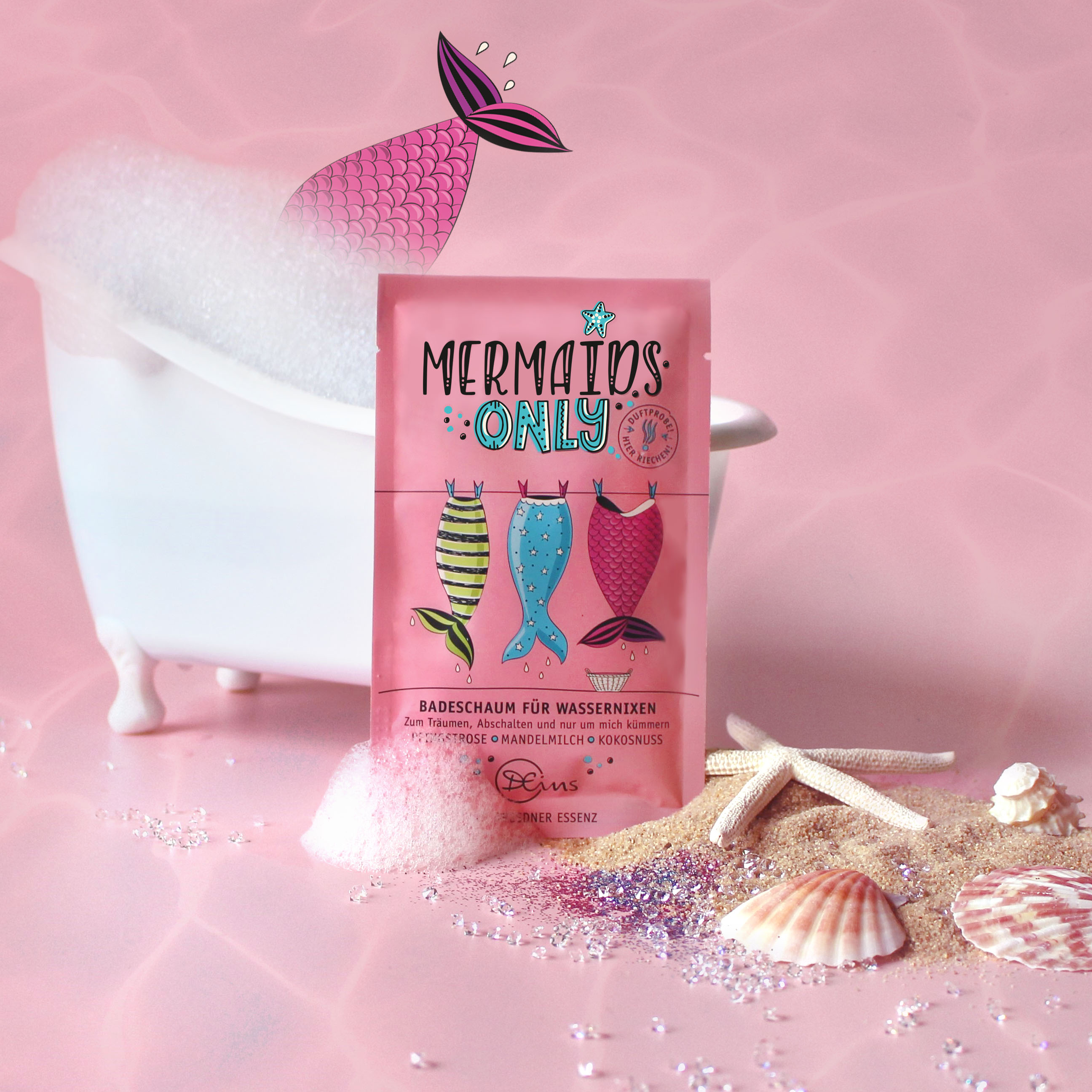 Mermaids only Badeschaum für Wassernixen steht vor einer schaeumenden Badewanne und daneben ist Sand und Glitzer verstreut und Seesterne und Muscheln platziert